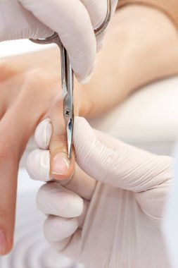 Manikürcünün manikür salonundaki kadın tırnaklarını sökmek için manikür makası kullanmasını kapat.
