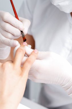 Lastik eldivenli manikür ustası güzellik salonundaki kadın tırnaklarına saydam oje sürüyor.