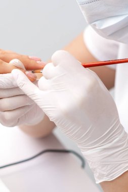 Lastik eldivenli manikür ustası güzellik salonundaki kadın tırnaklarına saydam oje sürüyor.