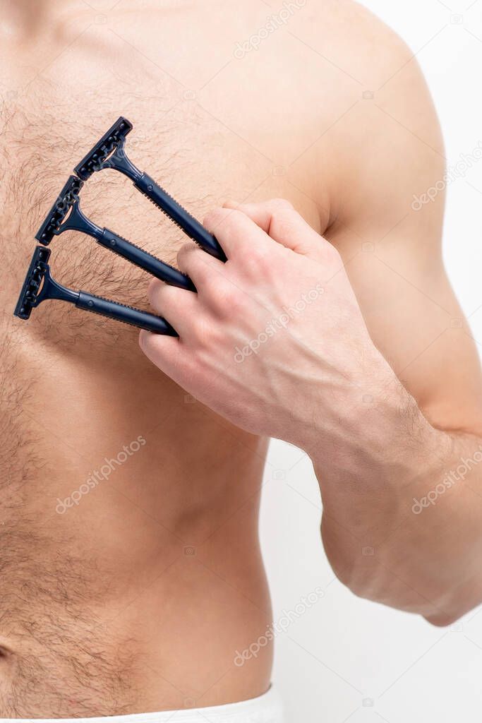 Young white man holds razor shaves on his chest on white background. Man shaving his torso