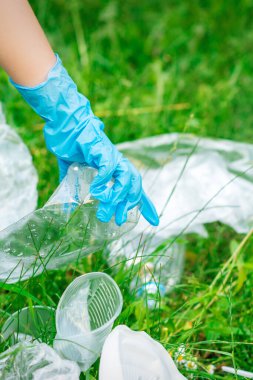 Çocuğun eli yeşil çimlerin üzerinde duran plastik enkazdan parkı temizler.