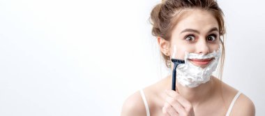 Beyaz arka planda jiletle yüzünü tıraş eden güzel beyaz bir kadın. Yüzünde tıraş köpüğü olan güzel bir kadın.