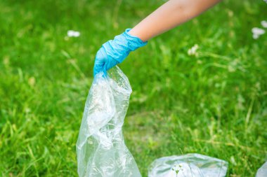Çocuğun eli yeşil çimlerin üzerinde duran plastik enkazdan parkı temizler.