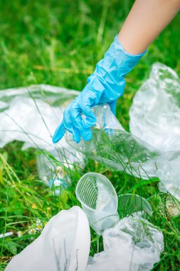 Çocuğun eli yeşil çimlerin üzerinde duran plastik enkazdan parkı temizler.