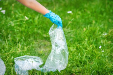 Çocuğun eli yeşil çimlerin üzerinde duran plastik enkazdan parkı temizler.