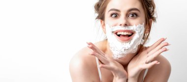 Yüzünde tıraş köpüğü olan beyaz arka planda poz veren güzel beyaz bir kadın.