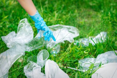 Çocuğun eli yeşil çimlerin üzerinde duran plastik enkazdan parkı temizler.