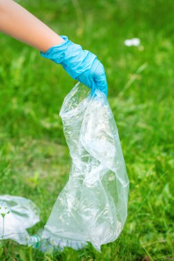 Çocuğun eli yeşil çimlerin üzerinde duran plastik enkazdan parkı temizler.