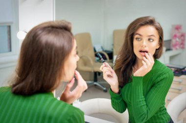 Güzel beyaz kadın, aynaya bakarak dudaklarına parmak ile parlatıcı sürüyor.