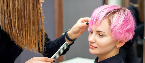 Young woman receiving short pink hairstyle by female hairdresser in beauty salon