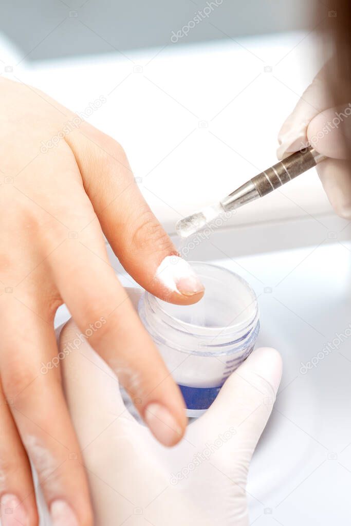Close up of the process of applying acrylic powder on the nails of a young woman in a beauty salon