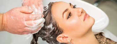 Güzel, genç, beyaz bir kadın kuaförde kuaförün erkek elleriyle saç yıkıyor.