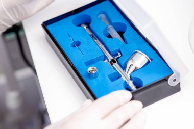 Manikür ustasının yakın çekimi, mavi kutudan alınan eldivenleri giyen tırnaklar için temiz bir hava fırçası çıkarıyor.