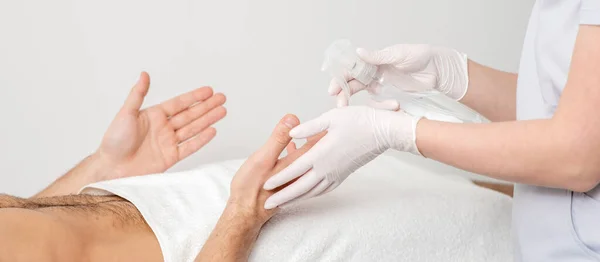 Nurse hand sanitizing hands of male patient in the hospital. Coronavirus protection concept.