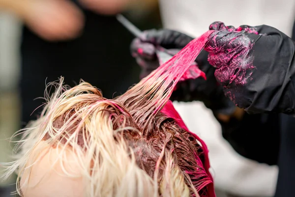 Close up shot of hair stylist dying hair of woman with pink dye in hair salon