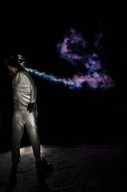 Beyaz keten kostümlü ve renkli dumanlı bir adam. Koyu arkaplan