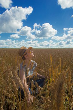 Kovboy şapkalı ve buğday tarlasında sarı güneş gözlüklü bir kadın.