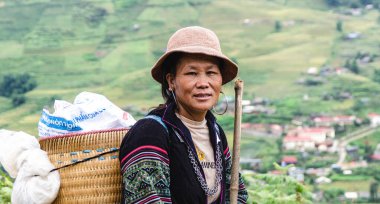 Sapa, Vietnam - 13 Eylül 2023 gülümseyen Vietnamlı kadın hasır sepet ve pirinç tarlalarında baston taşıyordu.