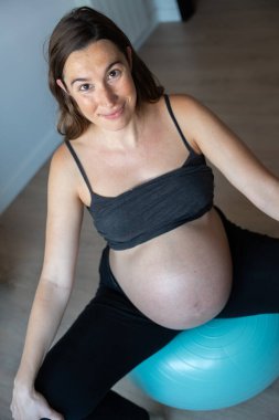 Evde pilates topuyla egzersiz yapan hamile bir kadının dikey resmi.