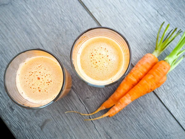 Fresh carrot juice in glass on a grey wooden table, Two glasses of homemade carrot juice with vegetables.