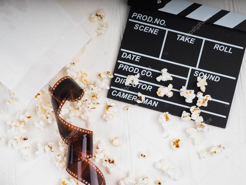 the film in the spiral, near the popcorn, Clapperboard copy space for text, fashion highlights in the photo, concept, film industry, film, abstract composition of movie, on a white background.