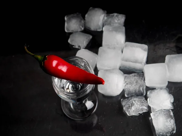 a shot of vodka, an alcoholic beverage, next to ice, fire, ice, red chili pepper. The concept of alcohol, spirits.