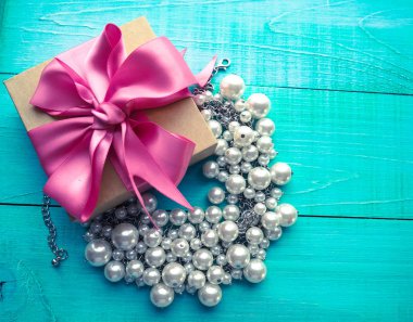 İnci mücevher mavi ahşap masa ve pembe kurdele yayla hediye kutusu.