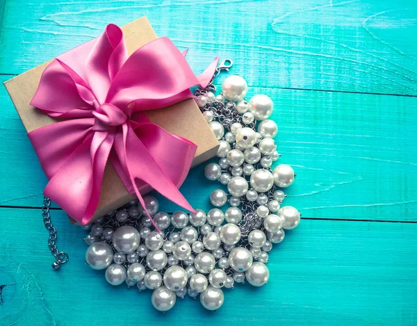 İnci mücevher mavi ahşap masa ve pembe kurdele yayla hediye kutusu.
