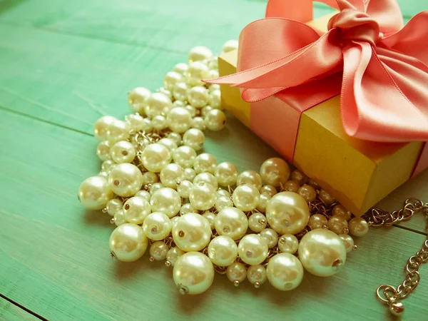 İnci mücevher mavi ahşap masa ve pembe kurdele yayla hediye kutusu.