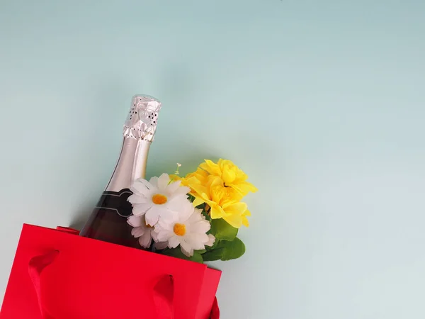 bottle of wine and flowers in the package on blue background, space for text.