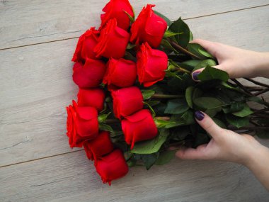 Güllerle tahta bir masada hediye hazırlıyorum. Kırmızı güllerin arka planında kurdele ile sarılmış bir hediye tutan kadın el, metnin altındaki boşluk.