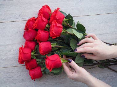 Güllerle tahta bir masada hediye hazırlıyorum. Kırmızı güllerin arka planında kurdele ile sarılmış bir hediye tutan kadın el, metnin altındaki boşluk.