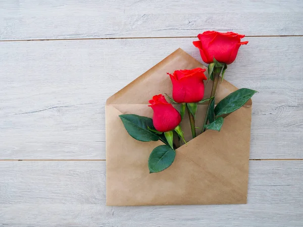 Envelop van kraftpapier, met bloemen-rode rozen op een houten ondergrond, ruimte voor tekst, als felicitatie huwelijk, verjaardag — Stockfoto