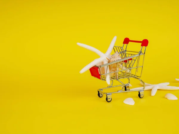 Carro de la compra, carro con conchas marinas sobre fondo amarillo . —  Fotos de Stock