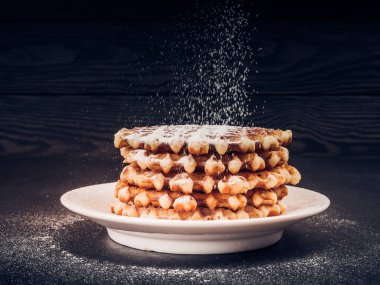 Beyaz plaka ile üstüne pudra şekeri siyah arka plan, çok lezzetli aperatif üzerine döktü eleme ev yapımı Belçika waffle. eski ahşap masa üzerinde şeker. Karanlık rustik tarzı. kopya alanı, şık
