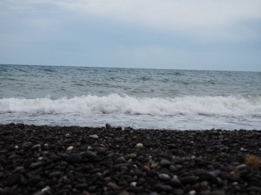 Çakıl sahilinde deniz dalgaları. Bulutlu bir yaz veya sonbahar gününde deniz
