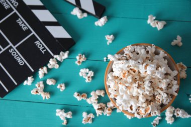 Mavi ahşap arka planda bir tabak patlamış mısır, üst görünümde, filmler için çırpınan pay 'ın yanında.