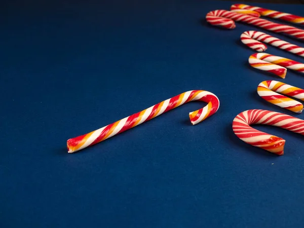 Christmas candy cane. On classic blue background. Flat lay. Christmas composition. A fan of caramel striped cane candies on a dark blue background. Minimalist New Year concept for your mockup