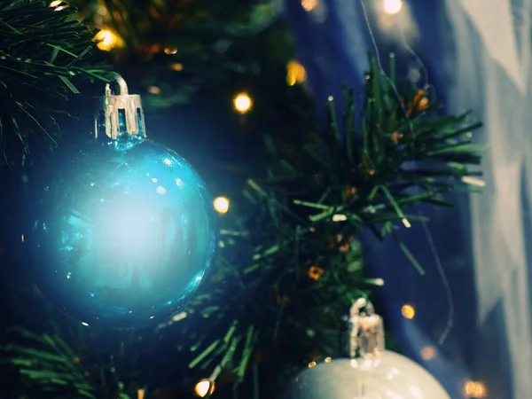 Close-up de Bauble pendurado na árvore de Natal iluminada. Bolas de Natal e bugigangas como fundo para cartões postais, muitos brinquedos de Natal diferentes em luzes sem foco, close-up — Fotografia de Stock