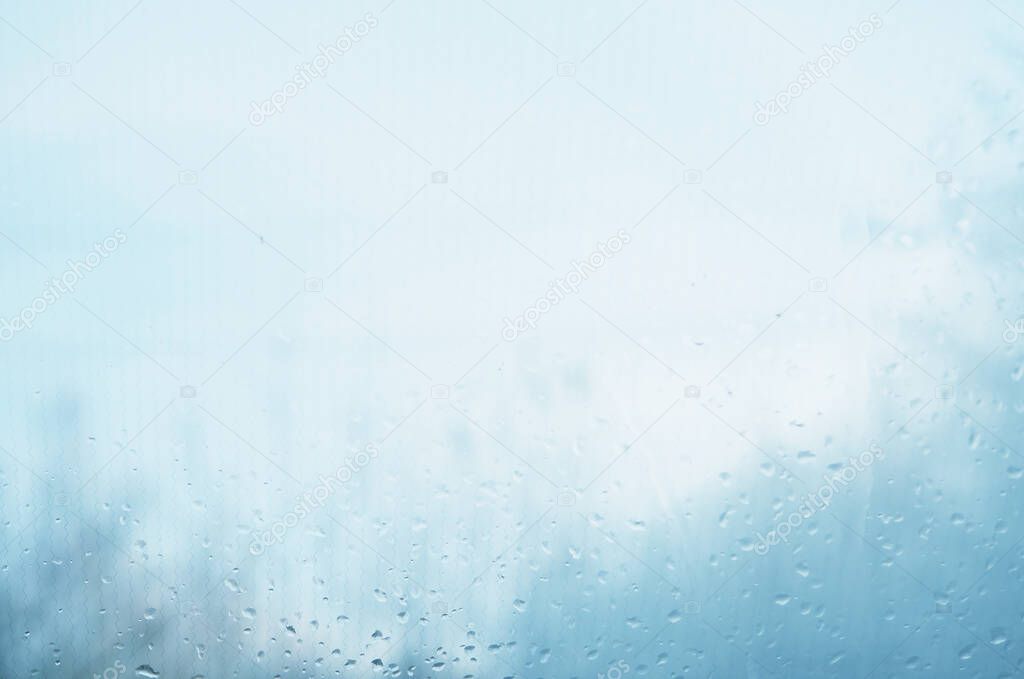 background selective focus, blurry, drops on the glass fuzzy, very blurry. Raindrops on window glass against blue sky with white clouds.