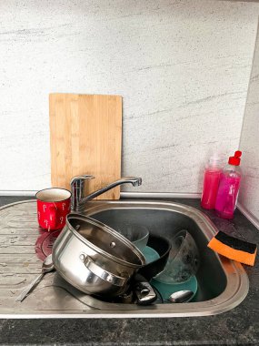 Kirli bulaşık, esrar, bardak, çatal bıçak, sünger ve deterjan dolu pis bir mutfak lavabosu. Ev temizliği ve ev işleri..