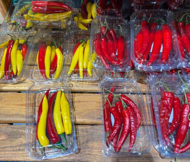 Taze kırmızı ve sarı kırmızı biberler süpermarketteki ahşap raflarda şeffaf plastik kutulara doldurulmuş. Baharatlı sebzeler, yemek pişirmek için doğal tarım ürünleri, acı sos ve egzotik yemekler..