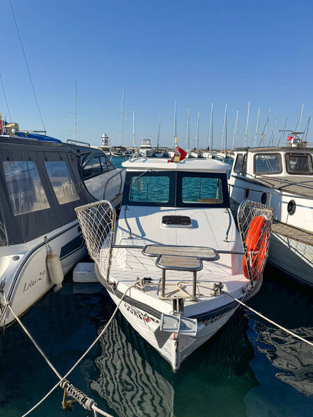 Editorial photo taken on June 30, 2025, in Izmir, Turkey. White motorboat docked in a marina among other boats with clear blue sky and masts in the background.