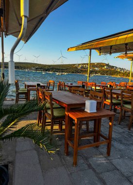 Türkiye 'nin İzmir kentindeki tepelerde boş ahşap masalar ve rüzgar türbinleriyle bir açık deniz kafesi manzarası. Fotoğraf 13 Eylül 2025 'te çekildi. Sadece editör kullanımı.