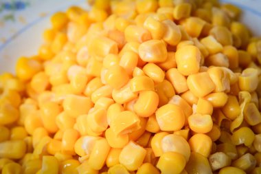 Beyaz bir tabakta düzgünce yerleştirilmiş sarı mısır tanelerinin fotoğrafı. Gıda ambalajı, editoryal kullanım veya aşçılık için temiz ve iştah açıcı bir bileşim