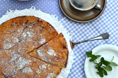 Ev yapımı meyve pasta ile bir fincan kahve ve nane masada, üstten görünüm.