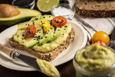 Taze avokado yayılmış Guacamole ve dilimleri kiraz domates ve bir parça ekmek üzerinde siyah susam ile. Sağlıklı kahvaltı konsepti.
