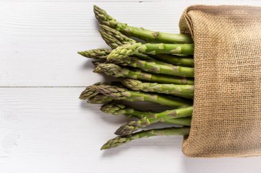 Juta çanta Beyaz ahşap masa üzerinde taze yeşil kuşkonmaz. Kopya alanı.