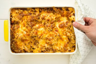 El ev yapımı et lazanya beyaz tahta masada sunmaktadır.