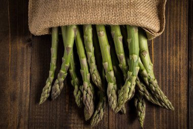 Juta çanta ahşap arka plan üzerinde taze kuşkonmaz